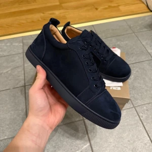 Mörkblå loubs storlek 43 - Snygga mörkblå sneakers från Louboutin i mocka med klassisk röd sula. Skorna har rund tå, snörning och diskreta detaljer på sidan. Perfekta för dig som vill ha en stilren och lyxig look med en touch av attityd.