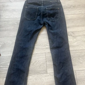 Mörkblå jeans med nitar på bakfickor - Snygga mörkblå jeans från Gina Tricot med raka ben och coola nitar på bakfickorna. Klassisk femficksmodell med knapp och dragkedja framtill. Perfekta för dig som gillar en stilren look med lite edge.