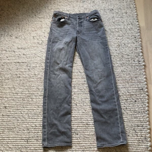 Grå Levi's 501 straight jeans - Säljer ett par grå Levi's 501 jeans med klassisk rak passform och fem fickor. Jeansen har en snygg tvättad look, silverfärgade nitar och tydliga sömmar. Ikonisk läderpatch bak i midjan och röd Levi's-tag på bakfickan. Perfekta till sneakers eller boots.