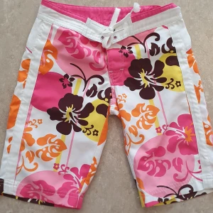Shorts - Snygga shorts från Lindex med stort blommigt mönster i rosa, orange, gul, brun och vitt. Shortsen har snörning i midjan och en bakficka med dragkedja. Perfekta för sommaren med sin färgstarka och somriga vibe.