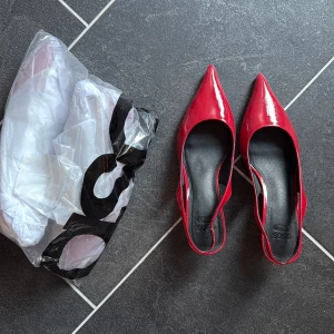 Röda taxklackar med spetsig tå  - Snygga röda pumps i lack från ASOS med spetsig tå och öppen häl. Köpte i två storlekar och glömde returnera de som var för stora… oöppnade och aldrig ens testade!