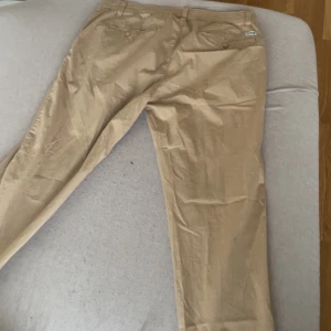 Beiga chinos i bomull - Snygga beiga chinos i klassisk rak modell. Byxorna har fickor både fram och bak samt hällor för bälte. Tillverkade i mjuk bomull som är skön att bära hela dagen. Perfekta för en clean och avslappnad stil. 32/32 