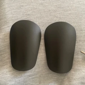 Minimalistiska Svarta Benskydd – Lätta & Slitstarka - 📄 Beskrivning: Säljer ett par svarta benskydd i stilren och minimalistisk design. ✔️ Lätta och bekväma ✔️ Perfekt för träning & match ✔️ Hållbart plastmaterial ✔️ Passar de flesta storlekar (ungdomar & vuxna). Helt nya !!! Pris kan diskuteras.