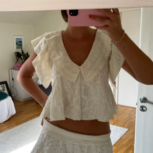 Vit blus med volangkrage och spets - Supersöt vit blus med stor volangkrage och v-ringning. Blusen har korta, luftiga ärmar och är dekorerad med broderade spetsdetaljer. Helt oanvänd 