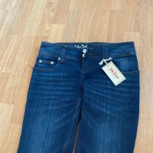 Mörkblå jeans från John Baner - Snygga mörkblå jeans från John Baner med klassisk femficksdesign och subtila slitningar. Jeansen har låg midja med  dubbla knappar och coola detaljer på bakfickorna. Perfekta för dig som gillar en tidlös och stilren look.