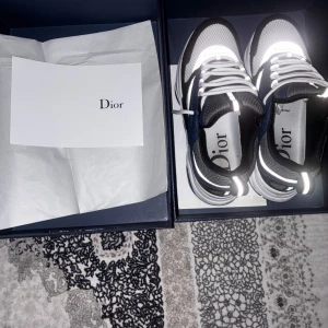 Dior sneakers i blått, vitt och svart - Snygga Dior sneakers med chunky sula i vitt, svart och blått. Skorna har meshdetaljer, reflekterande partier och vita snören. Insidan är märkt med Dior-logga och ovandelen kombinerar skinn och textil för en modern vibe.