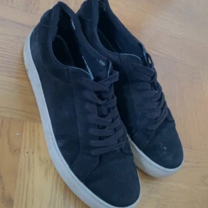 Svarta Vagabond - Svarta sneakers från Vagabond med ovandel i mocka och klassisk vit sula. Skorna har snörning och en stilren, rund tå. Perfekta för dig som gillar en clean och enkel look till vardags.