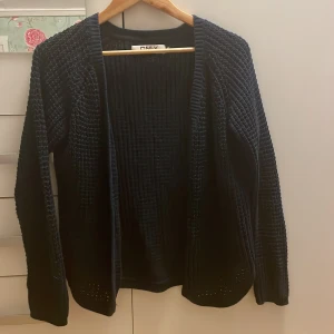 Svart stickad kofta från ONLY - Mysig svart stickad kofta från ONLY i storlek M. Koftan har öppen front, långärmad design och ett grovt stickat mönster som ger en cool struktur. Perfekt att slänga över en t-shirt eller topp för en chill look.
