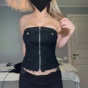 Svart jeanskorsett topp - Säljer en svart jeanskorsett eller jeanstopp med dragkedja i mitten. Dragkedjan har tyvärr ingen dragning-sak men den går att stänga ändå. Bak finns det stretch-tyg.