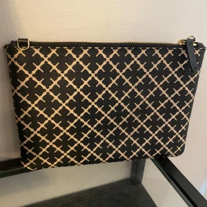 Kuvertväska från By Malene Birger - Snygg kuvertväska från By Malene Birger med svart och beige grafiskt mönster. Väskan har guldfärgad dragkedja och är tillverkad i tåligt syntetmaterial. Perfekt att bära i handen eller lägga i en större väska för extra stilpoäng. Utan axelbandet.