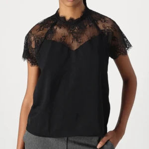 Svart blus med spetsdetaljer - Helt oanvänd tyvärr eftersom jag inte gillade den på mig. Jäääättefin annars och slutsåld! Svart blus med transparent spets upptill och på ärmarna. Hög hals med spetskant och korta ärmar ger en elegant vibe. Perfekt för dig som gillar en stilren look med extra detaljer. Blusen har rak passform och är lätt att matcha.