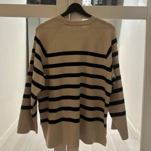 Beige och svart randig stickad tröja - Snygg stickad tröja i beige med svarta horisontella ränder. Tröjan har rund halsringning och långa ärmar, perfekt för lager-på-lager. Den har en avslappnad passform och är superenkel att styla till jeans eller kjol.