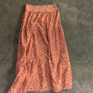 Rosa långkjol med paisleymönster och pärlor - INTRESSE KOLL På min långkjol från Zara. Flowy långkjol i ljusrosa med paisleyinspirerat mönster och snygga pärldetaljer i midjan. Kjolen har en avslappnad passform och är perfekt för vår och sommar. Materialet känns lätt och luftigt, vilket gör den superbekväm att bära hela dagen.