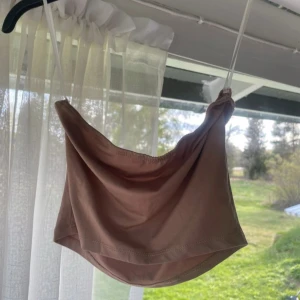 Beige bandeau tubtopp från SHEIN - Säljer en beige bandeau tubtopp från SHEIN i storlek XS. Toppen har en enkel och stilren design med tunna axelband och mjukt, stretchigt material som sitter skönt mot kroppen. Perfekt för varma dagar eller som layering-piece.