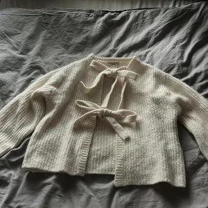 Beige stickad kofta med knyt från Gina Tricot - Superfin beige stickad kofta från Gina Tricot med två knytband framtill. Koftan har ribbade detaljer, lång ärm och en mjuk, mysig känsla. Perfekt för lager-på-lager och ger en söt touch till din outfit. Man kan även knyta upp banden💕