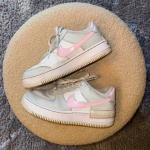 Nike Air Force 1 med rosa swoosh - Nike Air Force 1 sneakers i vitt och grått med ljusrosa swoosh och detaljer. Klassisk chunky sula, snörning och perforerad tå för extra ventilation. Ovandel i skinn och syntet, insida med orange Nike Air-logga. Perfekta för dig som gillar en clean men ändå lekfull stil. Nypris 1650kr, säljer för 499kr.