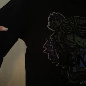 Svart Kenzo tröja - Svart tröja från Kenzo med ikonisk tigerbrodyr i lila, grönt och blått framtill. Tröjan har rund halsringning, ribbade muddar och lång ärm. 