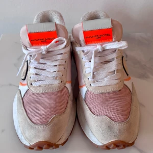 Philippe Model Paris sneakers i rosa och beige - Snygga Philippe Model Paris sneakers i mix av rosa, beige och vitt med detaljer i neonrosa och orange. Ovandel i mocka och textil, vit sula med grå detalj och logga på sidan. Skorna har snörning och en sportig vibe som sticker ut. Spår av användning/smuts på ovansidan. Se  bilder.