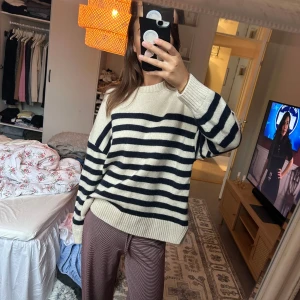 Randig stickad tröja i offwhite och svart - Säljer en oversized stickad tröja i offwhite med svarta horisontella ränder. Tröjan har rund halsringning, långa ärmar och breda ribbade muddar vid ärmslut och nederkant. Perfekt för lager-på-lager under kyliga dagar. Nypris: 1000kr 