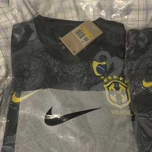 Nike Brasil CBF svart fotbollströja - Säljer en svart Nike fotbollströja för Brasilien med CBF-logga och ikoniskt motiv av Kristusstatyn på framsidan. Tröjan har korta ärmar, gul Nike-logga och detaljer i gult och blått. Tillverkad i Dri-FIT material som andas och passar perfekt för träning eller match. Storlek S och andra är för kids shorts ingår i kids storleken ålder 12-13 år 155-165cm. Tröjorna säljs för 300kr styck 