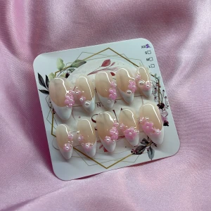 SugarSakura (XS);Medium Almond - Snygga gelé press on-naglar i en medium mandelform med fransk tipp. Naglarna är nude med vita toppar och dekorerade med 3D-blommor i rosa och små pärlor. Perfekt för dig som vill ha en söt och trendig look utan att gå till salong. Kommer i storlek XS: 14 mm, 11 mm, 11,5 mm, 10 mm, 8 mm 