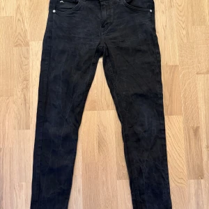 Svarta jeans från J.Lindeberg 33/32 - Svarta jeans från J.Lindeberg i klassisk femficksmodell. Byxorna har raka ben och normal passform, tillverkade i ett mjukt bomullstyg med lite stretch. Snyggt diskret J.Lindeberg-märke på bakfickan och läderpatch i midjan.