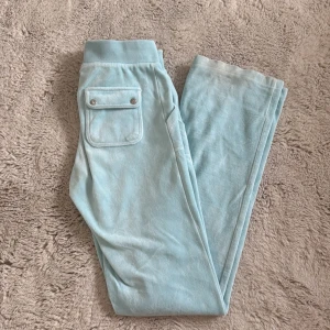 Ljusblå velourbyxor Juicy Couture XS - Supermjuka ljusblå mjukisbyxor från Juicy Couture i velour. Byxorna har raka ben, snörning i midjan och fickor både fram och bak med snygga detaljer. Perfekta för en chill och trendig look. Handuksmaterial. Har gått och trampat lite på de så de har blivit lite smuts som inte går bort i tvätten men det syns knappast.