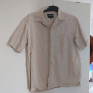 Beige kortärmad skjorta - Snygg beige skjorta från KappAhl i 100% bomull. Skjortan har korta ärmar, klassisk krage, bröstficka och knäppning framtill. Perfekt för en avslappnad och stilren look under varmare dagar. Använd sparsamt och pris går att diskuteras
