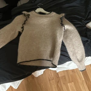 Beige stickad tröja med volangdetaljer - Superfin beige stickad tröja med svarta volangdetaljer.