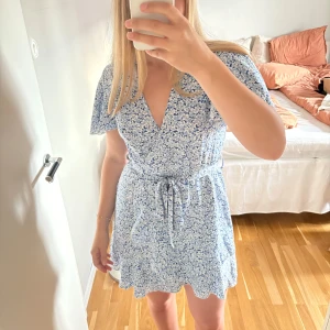 Blommig blå omlottklänning med volang - Blå, blommig omlottklänning med knyte i midjan. Mycket fin på sommaren. Vida ärmar och luftigt tyg. Fint skick! Storlek M men passar också S. Skriv gärna vid frågor🤗