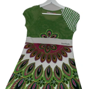 Färgglad kortklänning från Desigual - Superfin kortklänning från Desigual med grönt, vitt och rosa i ett unikt mönster. Klänningen har korta ärmar, asymmetrisk randig detalj på axeln och färgstarka grafiska tryck. Det står 13/14 men själv skulle jag säga att klänningen känns mindre.