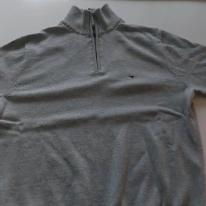Grå half zip tröja Tommy Hilfiger - Snygg grå tröja från Tommy Hilfiger med half zip och hög krage. Liten broderad logga på bröstet och ribbade detaljer vid halsen. Perfekt för lager-på-lager och chill stil. Materialet är mjukt och känns skönt mot huden. Knappt använd 2 gånger. 