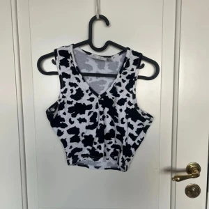 Svartvit croppad linnetopp Daisy Street - Cool croppad linnetopp från Daisy Street med svartvitt koskinnsmönster. Toppen har v-ringning och är ärmlös, perfekt för dig som vill sticka ut. Tillverkad i mjuk bomull med lite stretch för en skön passform.