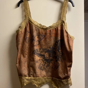 Brunt linne med spets och fjärilsmotiv - Säljer en brun linnetopp med gul spetskant och fjärilar på. Jättesöt motiv och bekvämt material. Säljer pga använder inte längre💕