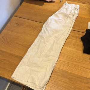 Beiga linnebyxor med resårmidja från H&M - Säljer ett par beiga linnebyxor från H&M med breda ben och elastisk midja. Byxorna har en avslappnad passform och är perfekta för varmare dagar. Lätta och luftiga med fickor i sidorna.