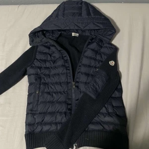 Moncler Cardigan - Säljer en mörkblå cardigan från Moncler med stickade ärmar. Jackan har dragkedja framtill, ribbade muddar och Moncler-logga på ärmen. Nfc skannen och allt övrigt är korrekt, det är bara att fråga ifall du funderar över något!