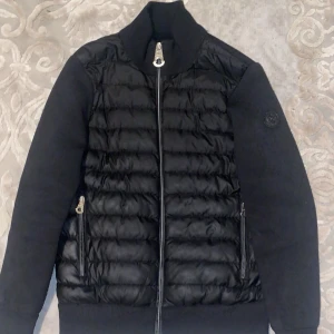 Svart cardigan från Moncler - Säljer en svart cardigan från Moncler med quiltad front och släta ärmar. Jackan har dragkedja framtill, två fickor med dragkedja och Moncler-logga på ärmen. Perfekt för kyliga dagar och riktigt snygg streetstil.