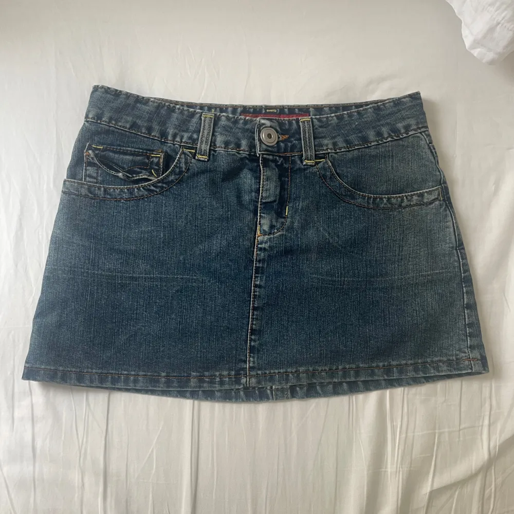 Säljer en klassisk blå jeanskjol med fem fickor och knappstängning fram. Kjolen har dekorativa sömmar och bakfickor med knappdetaljer. Perfekt för en avslappnad stil. Mått: midjemått tvärsöver 36.5cm, längd 29cm fram, längd bak 31.5cm. På etiketten står den ”40” men skulle säga att det är en Xs/S. Hameet.