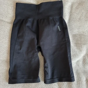 Svarta cykelshorts från Gymshark - Svarta cykelshorts från Gymshark med bred ribbad midja och diskret logga framtill. Tight passform och stretchigt material som passar perfekt för träning. Snygg och sportig look med hög midja.