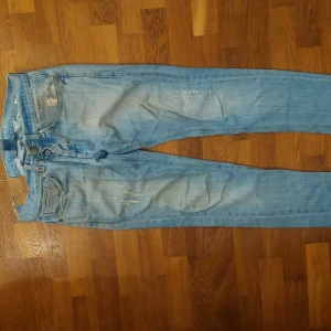 Ljusblå Dondup "George" jeans med slitningar - Säljer ett par ljusblå jeans med slitningar och lätt tvättad look. Klassisk femficksmodell. Jeansen har en rak passform och normal midja.