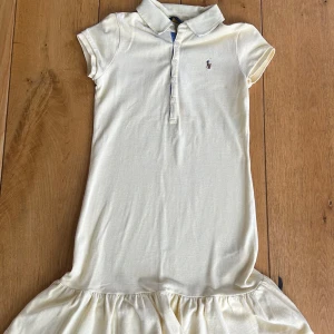 Gul pikéklänning från Polo Ralph Lauren - Säljer en klassisk gul pikéklänning från Polo Ralph Lauren med krage, korta ärmar och volang nertill. Storlek barn M eller 8-10 år.