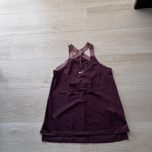 Vinröd träningstopp från Nike - Säljer en vinröd träningstopp från Nike med brottarrygg och meshmaterial för extra ventilation. Toppen har ett litet vitt Nike-logga framtill och är perfekt för gym eller löpning.