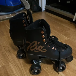 Svarta rullskridskor från Rio Roller - Säljer ett par svarta rullskridskor från Rio Roller med snygga gulddetaljer och snörning. Fina guld hjul med Rio loggan och använda sparsamt. Ganska nya och om man vill kan jag tvätta innan leverans.