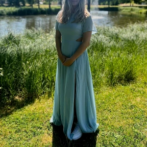Ljusblå långklänning med slits och cut-out - Säljer en ljusblå långklänning med korta ärmar och snygga cut-out detaljer i midjan. Klänningen har en elegant slits framtill och ett luftigt fall, perfekt för sommarens tillställningar. Köpt för 800kr andvänd 1 gång