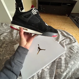 Svarta Nike Air Jordans med vita och röda detaljer - Säljer ett par svarta Nike Air Jordans med vita och röda detaljer. Skorna har nätpaneler på sidorna, vita snörhål och en synlig luftdämpning i sulan. Klassisk design med rund tå och platt sula. Perfekta för dig som gillar streetwear.