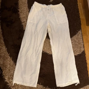 Vita linnebyxor med dragsko - Säljer ett par luftiga vita linnebyxor med resår i midjan och dragsko vid bensluten. Perfekta för varma dagar och har en avslappnad passform. Byxorna är helt nya och oanvända därför säljs dom för samma pris jag köpte på rea alltså 120kr!