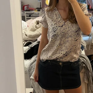 Silkesblus med puffärm - Säljer en beige blus med svart abstrakt mönster och korta puffärmar. Blusen har v-ringning och är tillverkad i ett lätt material som passar perfekt till både jeans och kjol. Säljer även kjolen