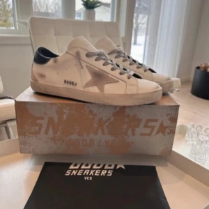 Golden Goose Superstar sneakers  - Golden Goose Superstar sneakers i vitt skinn med grå stjärndetalj på sidan och svarta hälpartier. Skorna har grå snörning och en klassisk rund tå. Snygg vintage-look med slitna detaljer och platt sula. De är nästan helt nya och bara använda en gång. Säljer pga att de var för små. Kan gå ner i pris för snabb affär. Storleken är 42 men skulle säga att de passar 43. Kan gå ner i pris för snabb affär