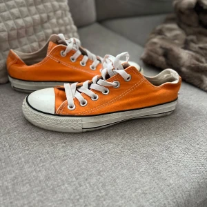Orangea Converse All Star sneakers - Säljer ett par klassiska Converse All Star sneakers i orange med vita snören och tå. Skorna har låg modell, rund tå och vit sula med svart rand. Perfekta för dig som vill sticka ut med färg på fötterna!