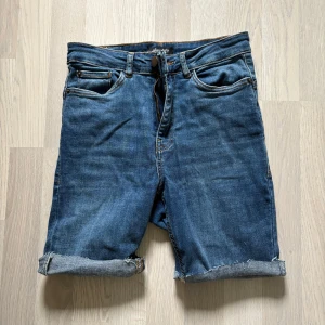 Avklippta Jeansshorts från Happy Holly - Avklippta Snygga blå jeansshorts från Happy Holly med klassisk femficksdesign och uppvikta benslut. Perfekta för varma dagar och enkla att matcha med olika toppar. Stängs med knapp och dragkedja. Midjemått ca 33 cm